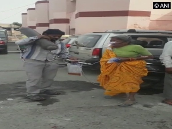 Man awaits ambulance while carrying mother's oxygen cylinders on shoulder