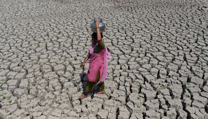 A woman walks on the parched bed of Chandola Lake with a metal pot on her head to fetch water in Ahmedabad on 20 May 2016. India is facing its worst water crisis in decades, with about 330 million people  suffering from drought
