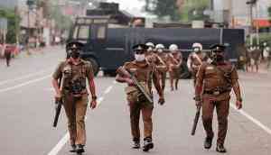 Sri Lankan police officers with tear gas guns walk along a main road as people protest